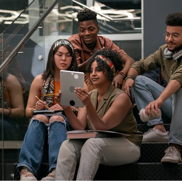 A group of students gathered on a staircase, looking at a tablet together