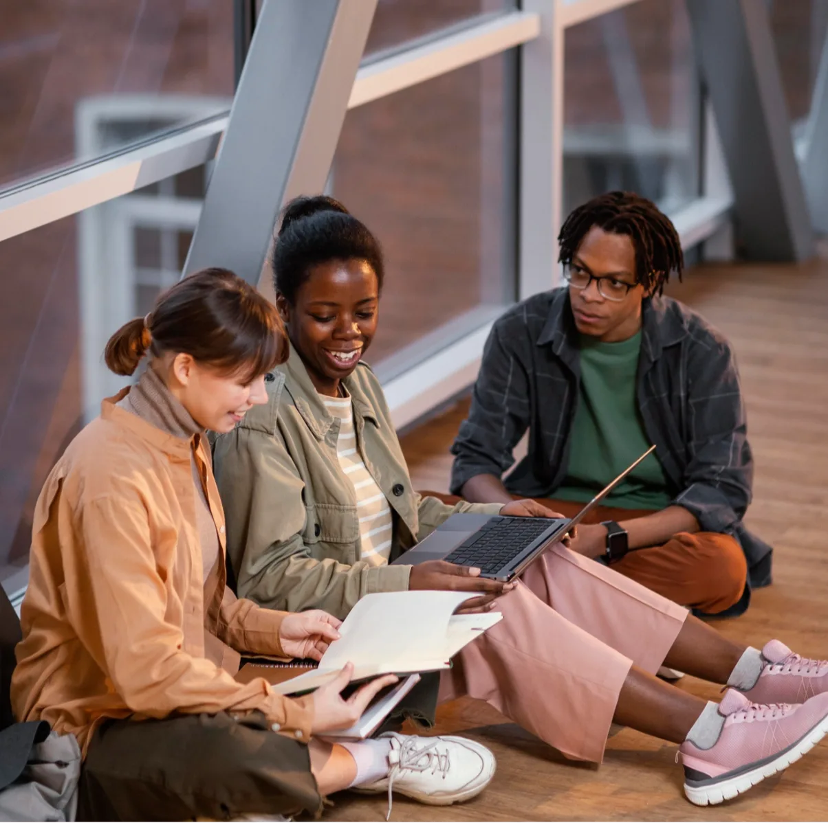 Three students sitting together, studying with a laptop and notebook